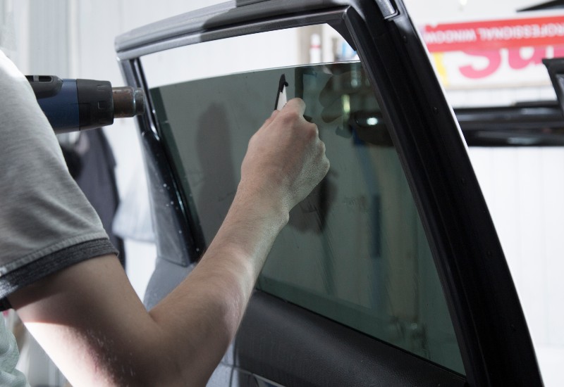 Worker Applying Dark Window Tint on a Car for Improved Comfort and Style in Orlando